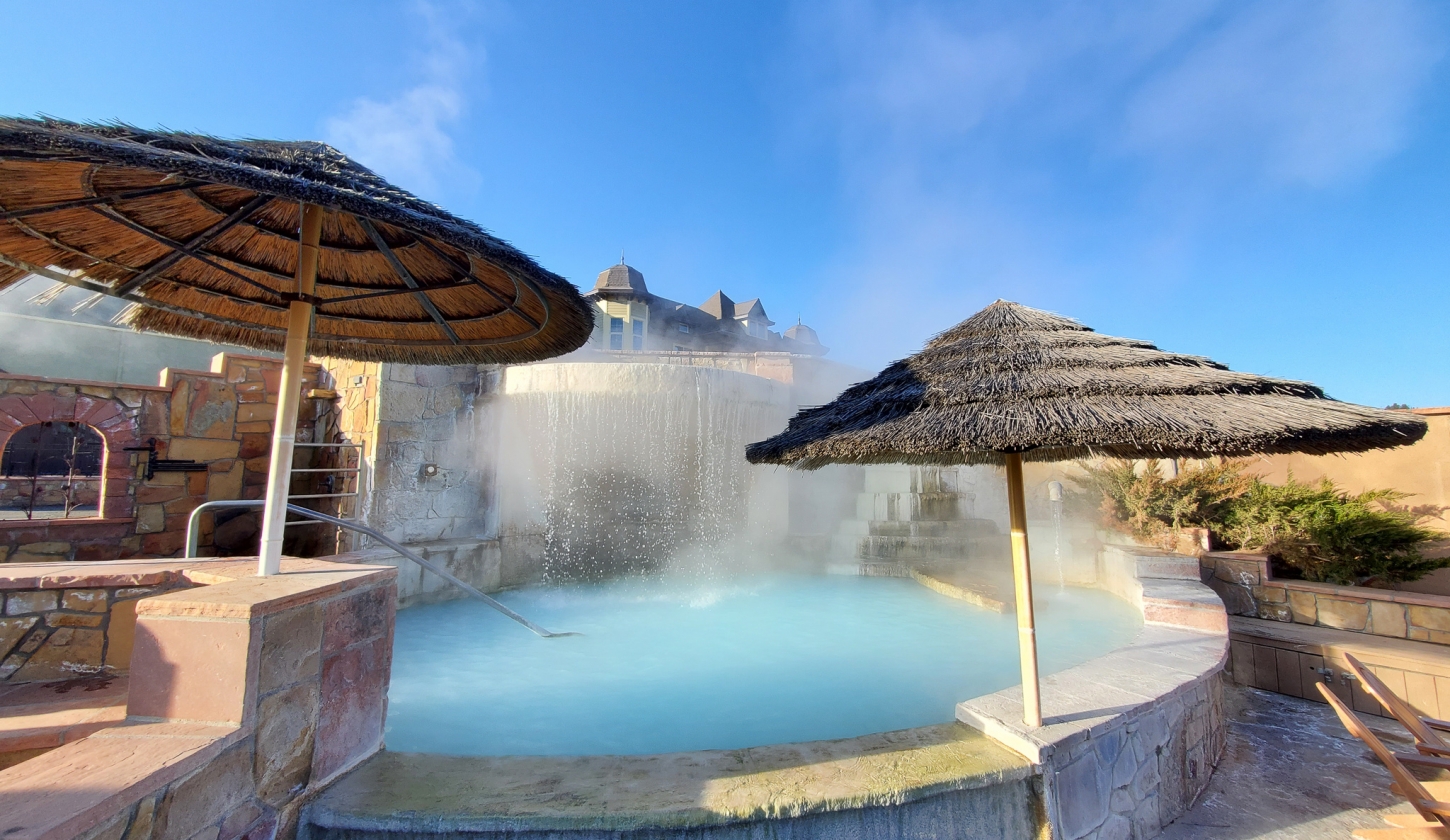Waterfall filling the hot spring pool lined with thatched umbrellas