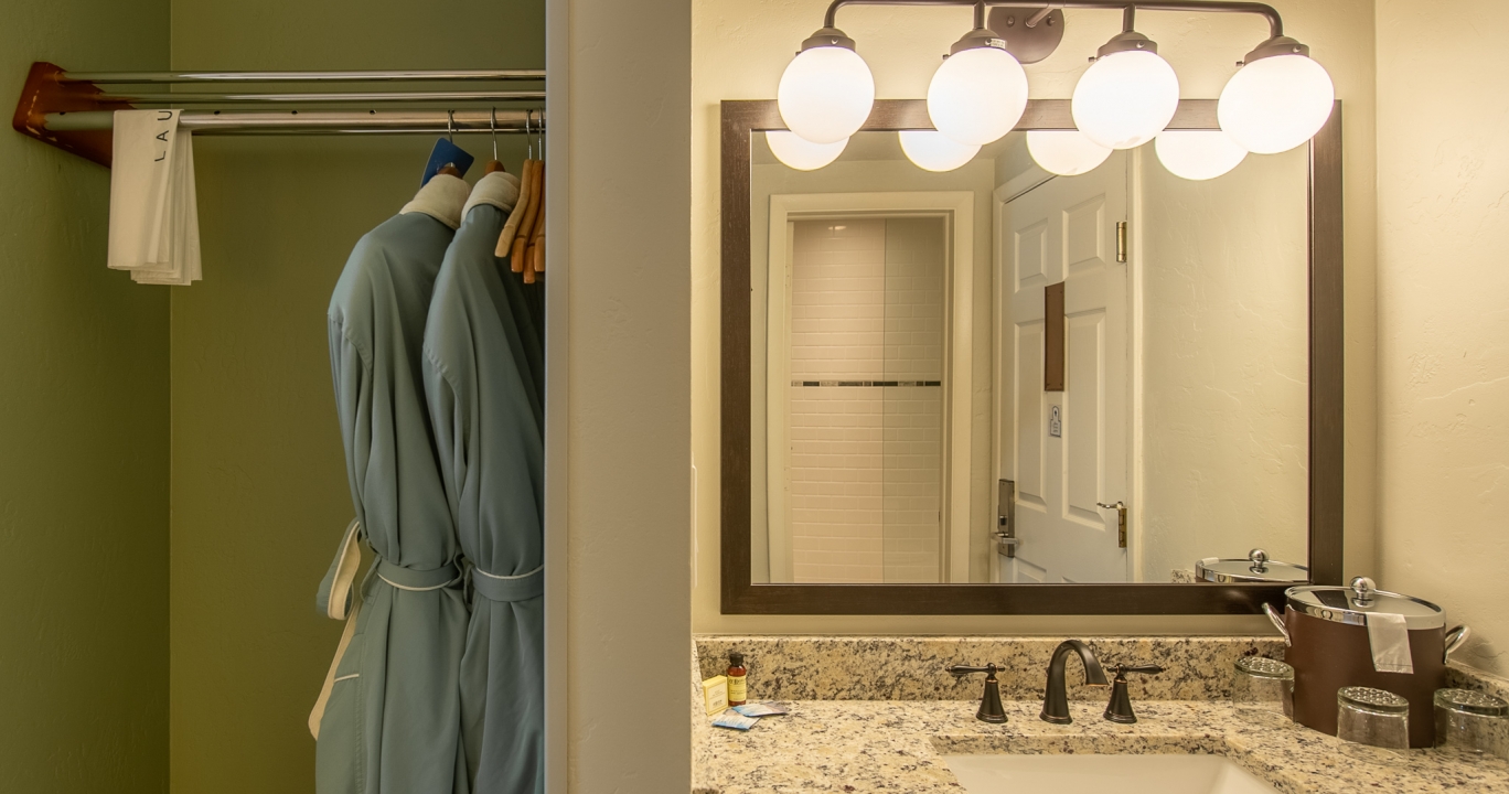 A pair of robes hanging next to a bathroom marble countertop sink with quadruple cluster light