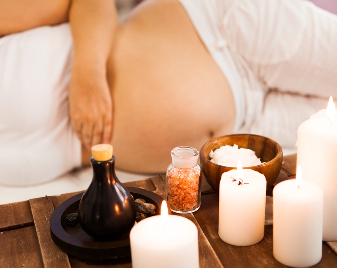 A pregnant women lying on her side next to a table with candles, bath salt and essential oil