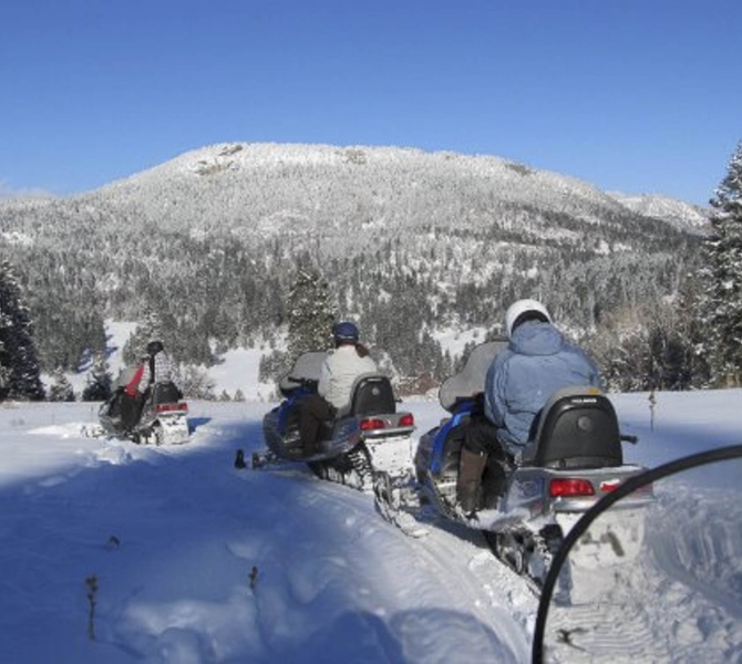A group riding snowmobiles outdoors during winter