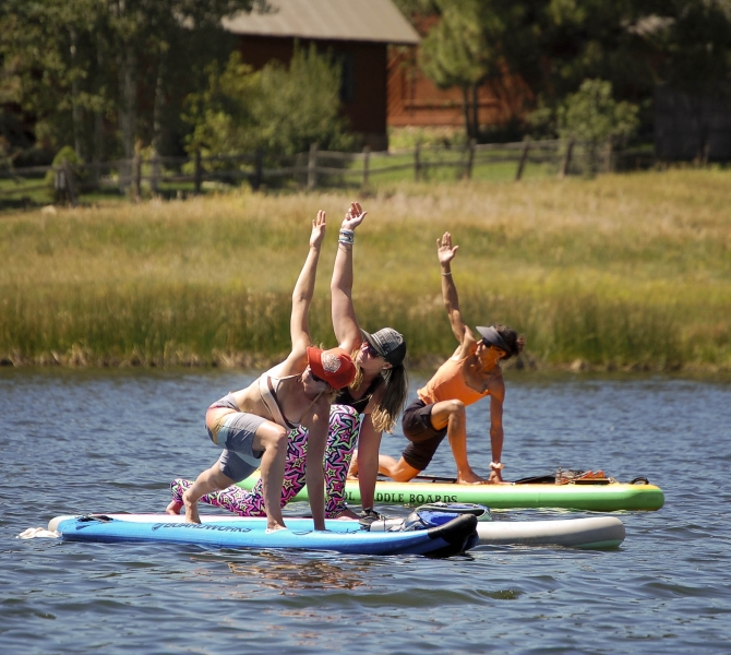 Three women stretching on their paddle boards in the water
